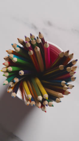 Vertical-Video-Overhead-Shot-Of-Multi-Coloured-Pencils-In-Pot-On-Marble-Background-With-Person-Choosing-Pink-Pencil